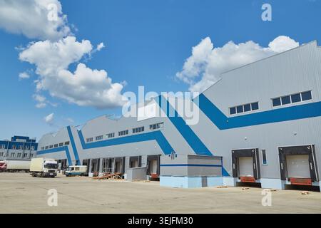 Exterior facade of a large, modern warehouse or distribution center with grey and blue metal siding, multiple loading docks, and roll-up doors, under Stock Photo