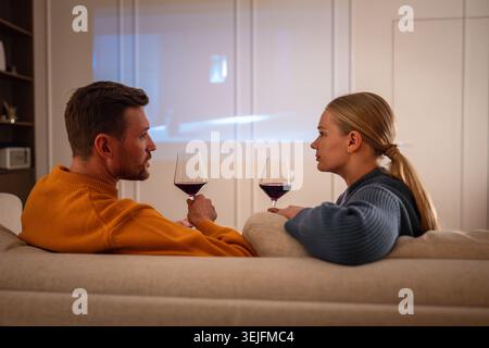 Couple gazing at each other during romantic movie night with projector cozy setting on sofa at home Stock Photo