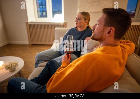 Relaxed family resting on sofa watching TV while drinking alcohol and eating snacks at home Stock Photo