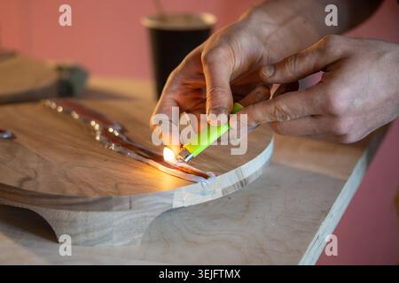 Carpenter hands removing air bubbles from liquid epoxy resin in wood crack using lighter flame Stock Photo