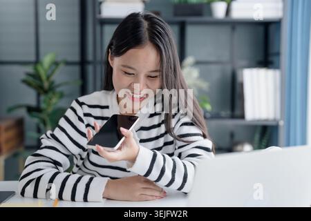 Asian Woman Engaging with Voice Assistant on Smartphone in Modern Home. Stock Photo