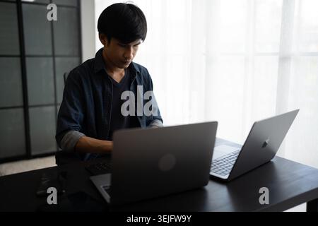 Asian man software engineer Working on Computer at office desk for writing program code IT Software Engineer finding errors tech support devops creati Stock Photo