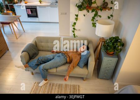 Exhausted mature woman lying on couch in solitude, dealing with migraine, depression and apathy Stock Photo