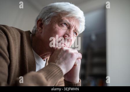 Thoughtful serious sad elderly man resting head on arms looking into distance with detached gaze Stock Photo