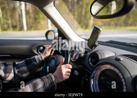 Closeup of woman hands holding steering wheel driving car, using navigation app on smartphone. Stock Photo