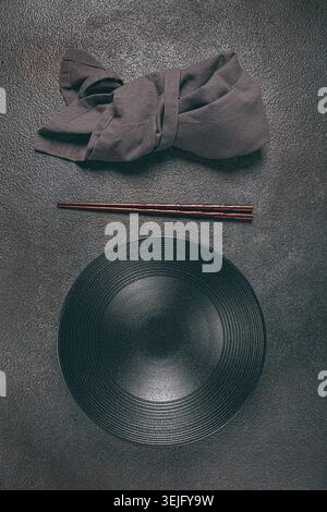 Empty black bowl and chopsticks, cloth napkin, top view, vertical, on a dark background, Stock Photo