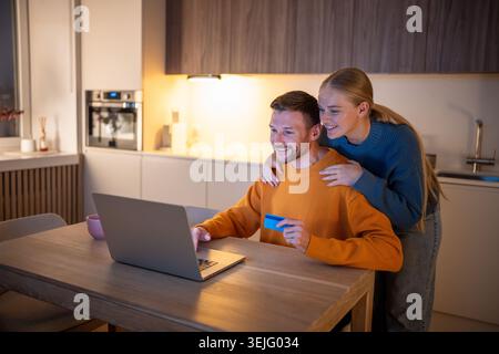 Middle-aged couple making purchases and reservations online using laptop and paying by card Stock Photo