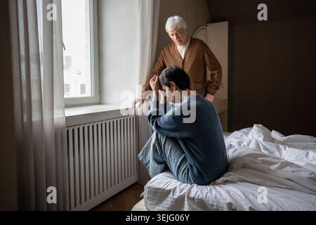 Grieving woman hiding face in hands. Compassionate sad husband comforting her on bed, couple loss Stock Photo