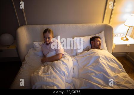 Unhappy sleep deprived woman lying awake in bed due to husband snoring in shared bedroom, insomnia Stock Photo