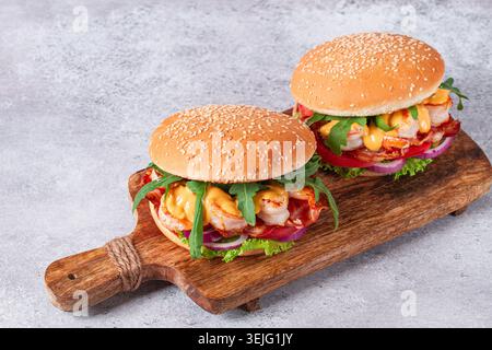 Shrimp burgers with fresh ingredients are served on a wooden board in a bright kitchen, Stock Photo