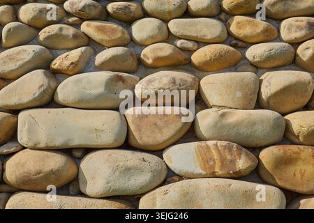 Close-up texture of smooth, naturally shaped river stones and pebbles forming a decorative surface or background pattern. Stock Photo