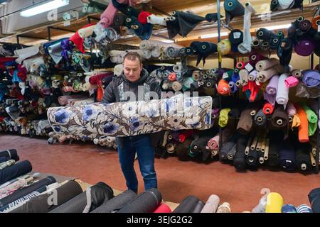 A Designer carries a roll of floral fabric in a warehouse filled with textiles. This image is perfect for illustrating the textile industry, fabric se Stock Photo