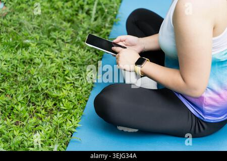 fit young asian woman using phone checking fitness applications standing in green nature park outdoor Stock Photo