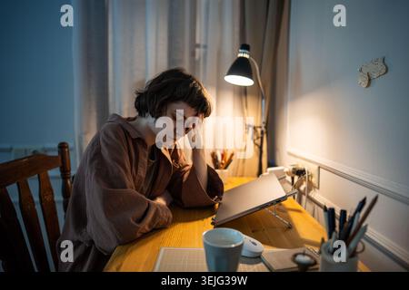 Exhausted woman sitting at home work desk with head in hand, feeling headache and unable to work or study. Stock Photo