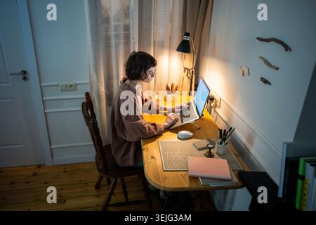 Focused busy woman working late. Tired concentrated young female typing laptop at home at night Stock Photo