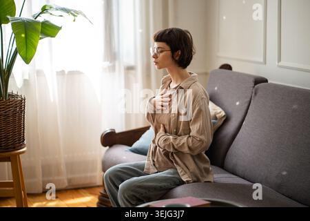 Meditating young woman with hands on chest practicing deep breaths to manage stress and anxiety Stock Photo