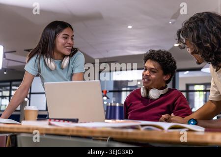 Diverse students studying together at communal table with silver laptop, headphones, coffee cup Stock Photo