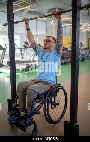 Disabled man in wheelchair doing vertical pull ups in sports center on post injury recovery session. Stock Photo