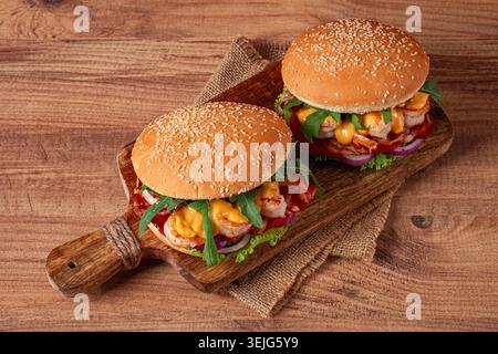 Two shrimp burgers and buns with sesame seeds, bacon, lettuce, tomatoes and onions,on a wooden board, rustic style, Stock Photo