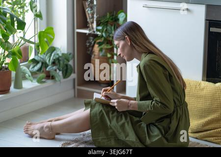 Happy middle aged woman writing down notes and ideas in personal diary, gratitude journal therapy. Stock Photo
