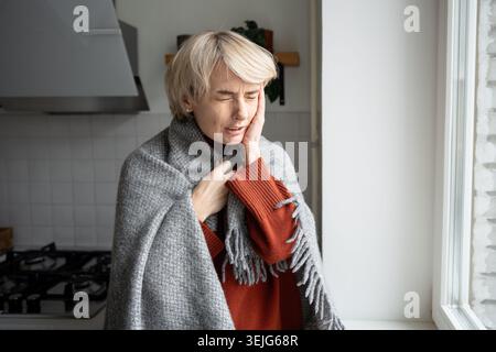 Middle aged woman with painful expression suffering from migraine or tooth pain, having headache. Stock Photo