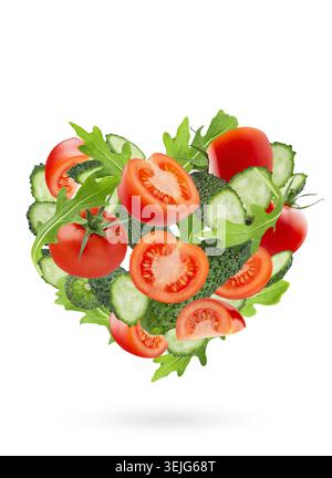 Fresh vegetables as heart shape. Salad ingredients - red tomatoes, cucumbers, leafy greens flying on white background as heart. Stock Photo