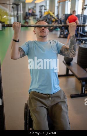 Determined athlete in wheelchair doing vertical pull ups during post injury rehabilitation at training session in sports center. Motivated man working Stock Photo