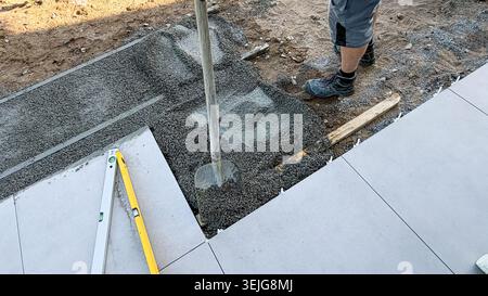 Construction worker using a concrete vibrator to level freshly poured concrete on a construction site with tools and gravel visible in the background Stock Photo
