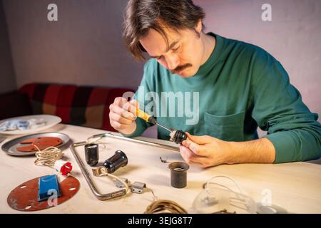 Craftsman at workshop unscrewing with screwdriver tool light bulb socket parts from vintage lamp. Stock Photo