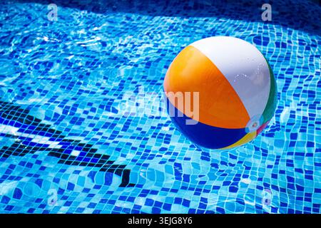Colorful beach ball floats on the surface of a pool reflecting sunlight on a summer day Stock Photo