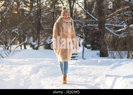 Woman walking on snow path in park at sunny frosty day, enjoying winter moments and nature Stock Photo