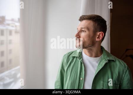Thoughtful man looking at window with calm expression, contemplating ideas and finding inspiration. Stock Photo