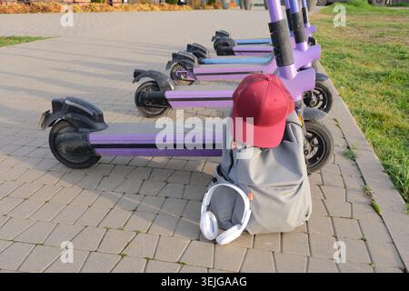 Backpack, cap and white headphones on electric scooters parking background Stock Photo