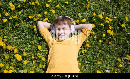 Preteen boy wearing headphones listens to music lying on the grass Stock Photo