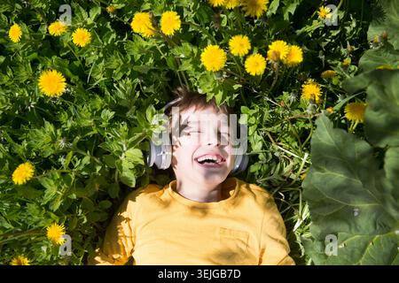 Preteen boy wearing headphones listens to music lying on the grass Stock Photo