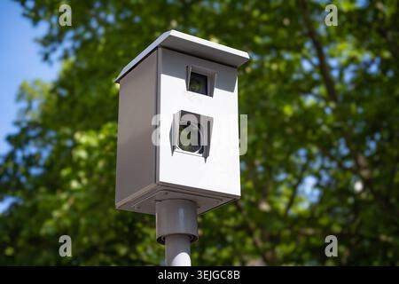 Traffic speed camera mounted on a pole outdoors with green trees and blue sky in the background Stock Photo