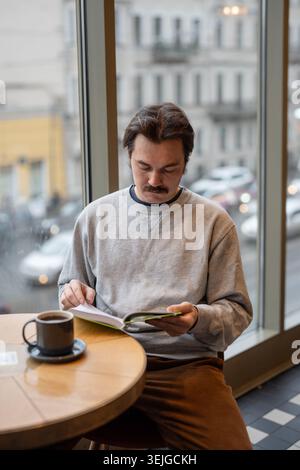 Stylish handsome man reading favorite book while sitting in cozy coffee shop during day break. Stock Photo