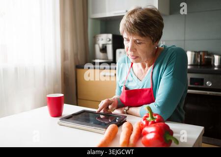 Elegant elderly woman using  tablet in the kitchen Stock Photo