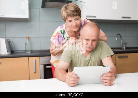 Happy senior couple using tablet in kitchen at home Stock Photo