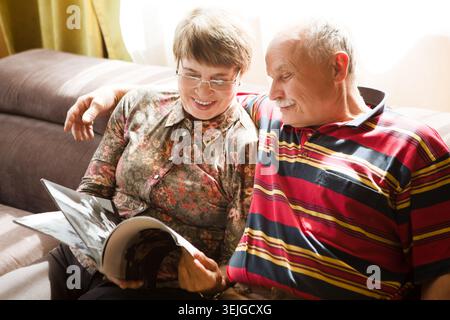 Happy senior couple sitting on sofa and reading a magazine in living room Stock Photo