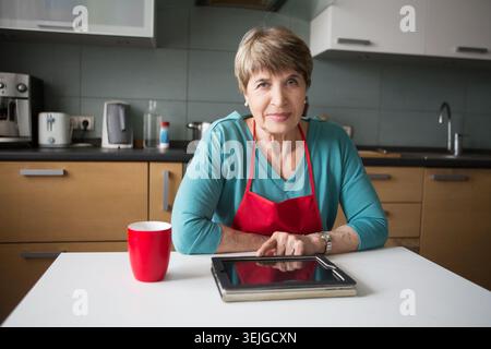 Elegant elderly woman using  tablet in the kitchen Stock Photo