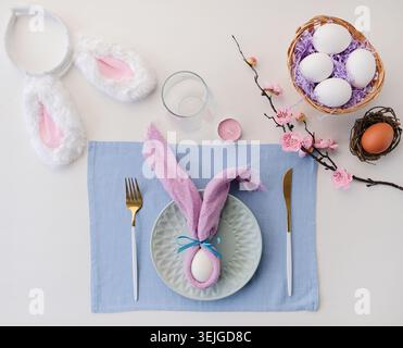 Easter table setting, egg with bunny ears on plate on the table decorated for Easter, top view Stock Photo