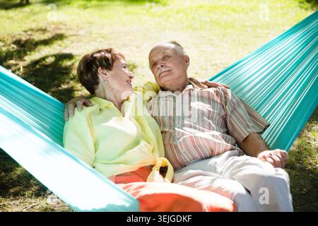 Happy senior couple rest in a hammock in a summer park or garden. Concept of friendly family. Stock Photo