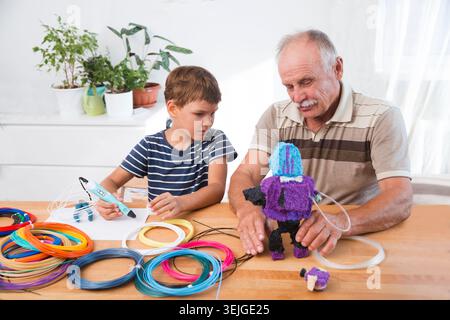 Grandparents spend time with their grandchildren at home. Kid boy and his drandfather using 3d printing drawing pen. Creative, l Stock Photo