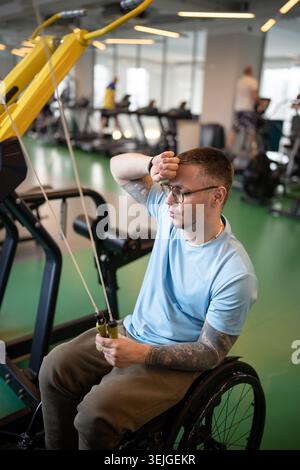 Disabled man athlete with spinal injury doing upper body exercise in gym at rehabilitation session. Stock Photo