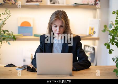 Relaxed business woman working on laptop in casual cafe, typing information or doing research. Stock Photo