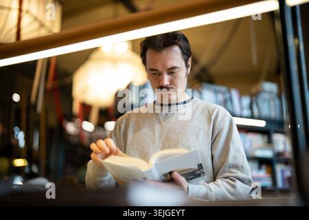 Focused man booklover reading book in modern bookshop, flipping through pages, enjoying novel. Stock Photo