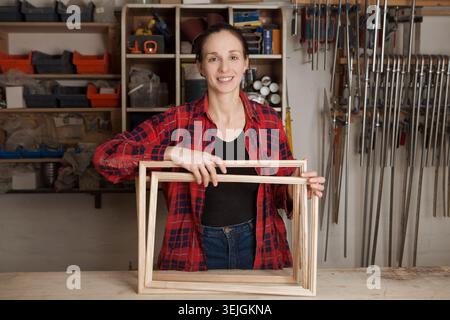 Woman carpenter wearing working clothes and smiling in her workshop. Stock Photo