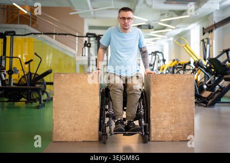 Determined disabled male in wheelchair doing upper body push ups workout using wooden blocks. Stock Photo