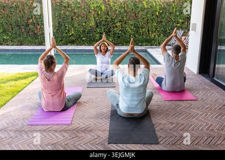 Diverse group following senior instructor practicing yoga on herringbone patio mats beside pool. Outdoor, mindfulness, serene, s Stock Photo